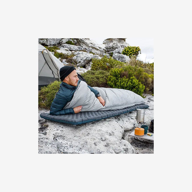 Backpacker relaxing on R3.5 pad next to campfire in chilly mountain terrain