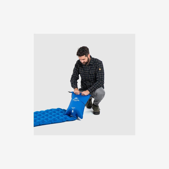 Camper inflating sleeping pad with inflator dry bag during camp setup